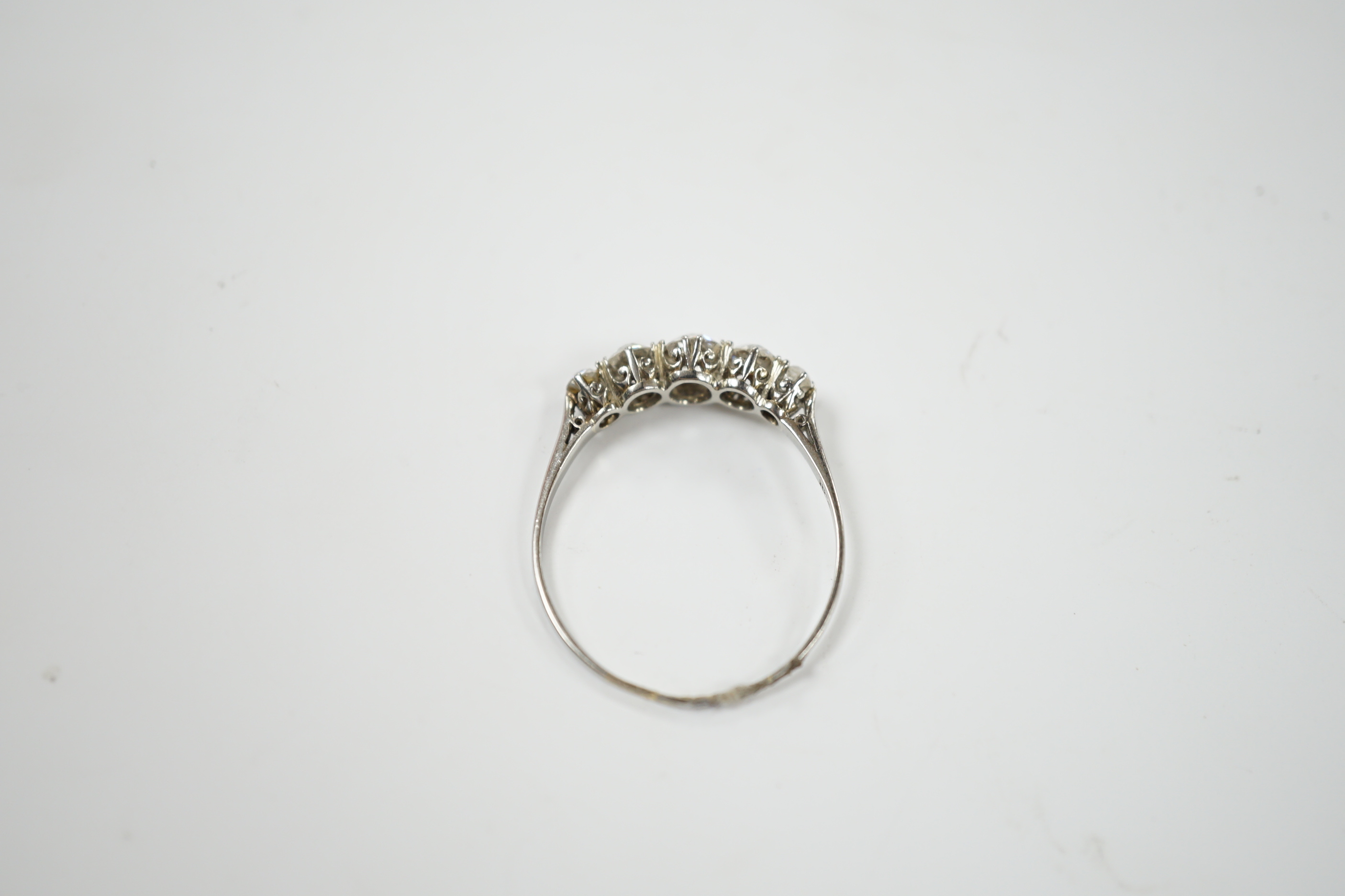 An 18ct white metal and graduated five stone diamond set half hoop ring, size X/Y, gross weight 2.2 grams.